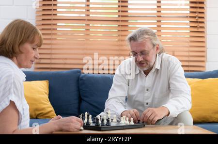 Im Wohnzimmer des Hauses sitzt ein älteres Paar und entspannt sich. Um gemeinsam mit einem Schachbrett Schach zu spielen. Stockfoto