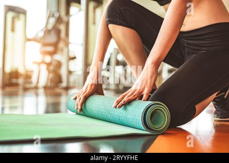 Nahaufnahme der sportlichen Frau faltende Yoga-Matratze im Sport-Fitness-Gym-Trainingszentrum Hintergrund. Trainingsmatte rollt nach hinten Stockfoto