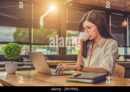 Asiatische arbeitende Frau, die Laptop benutzt und Kaffee im Café trinkt. Das Konzept der Menschen und Lebensstile. Technologie und Geschäftsthema. Kostenlos Stockfoto