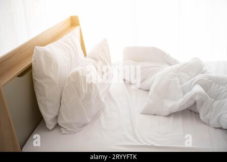 Weißes, ungebautes Bett am Morgen mit Sonnenschein mit weißem Vorhanghintergrund in elegantem Haus. Inneneinrichtung und luxuriöse Möbel Stockfoto