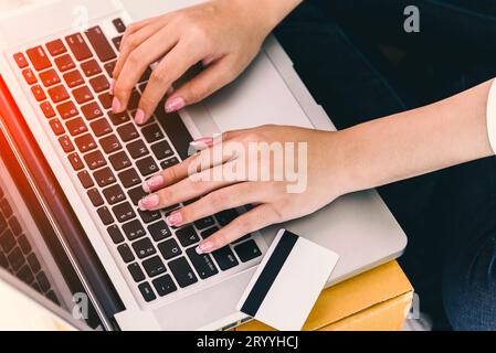 Nahaufnahme der Hände einer Frau, die einen Laptop mit Kreditkarte neben dem Computer benutzt. Technologie- und Lifestyles-Konzept. Thema „Geschäftsfrau“. Stockfoto