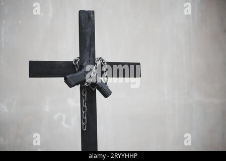 Schwarzes Kreuz mit Kette und Pistole an weißer Grunge-Wand. Objekt- und Waffenkonzept. Thema christliche Religion. Halloween und Crim Stockfoto