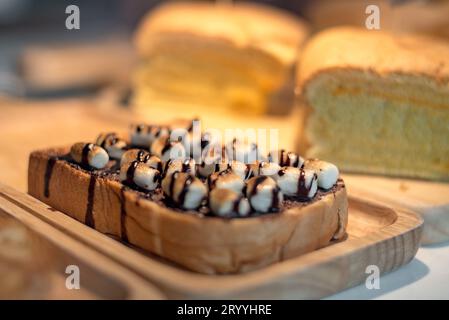 In Scheiben geröstetes Brot mit marshmello-Belag mit Schokoladensoße auf Holzteller. Essen und Getränke Konzept. Bäckerei und Kaffeespezialitäten Stockfoto