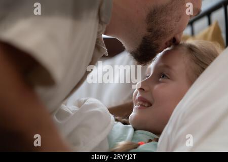 Bevor er sich in die Nacht zurückzieht, drückt ein Vater seine Zuneigung aus, indem er seiner Tochter auf die Stirn küsst. Um eine erholsame Nacht zu bekommen Stockfoto