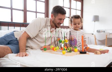 Vater und kleines Mädchen haben Spaß beim Spielen mit deinen neuen Spielzeugen im Schlafzimmer. Spielzeug, das das Denken von Kindern fördert Stockfoto