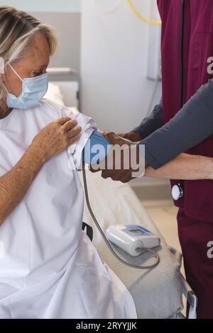 afroamerikanischer Arzt, der den Blutdruck des älteren Kaukasier-Patienten misst, der Gesichtsmasken trägt Stockfoto