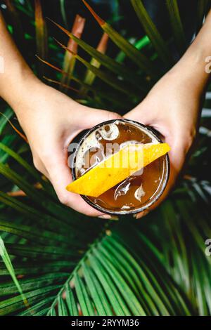 Orange Americano Iced Coffee in der Hand halten. Eisschwarzer Kaffee gemischt mit Orangensaft auf dem Tisch Stockfoto