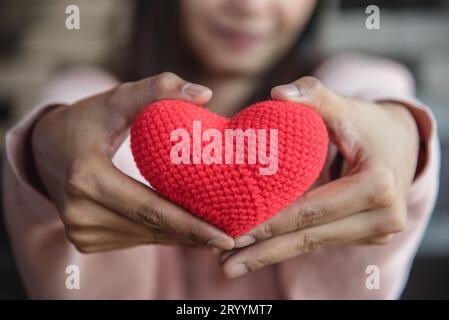 Großes rotes Garn, das Herz hält und mit der Frauenhand nach vorne gibt. Liebe und Zuneigung im Valentinstag-Konzept. Romantisches Objekt und Stockfoto