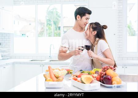 Asiatische Liebhaber oder Paare trinken Wein in der Küche zu Hause. Liebes- und Glückskonzept Süße Flitterwochen und Valentinstag Stockfoto