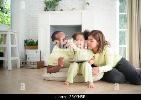 Kleine Kinder spielen und lernen Dinge in der weiten Welt auf einem Tablet. Mit Eltern, die im Wohnzimmer des helfen Stockfoto