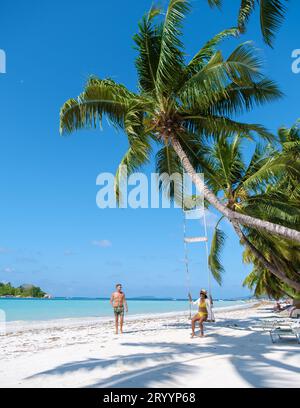 Ein paar Männer und Frauen an einem tropischen Strand mit Schaukel unter einer Palme Stockfoto