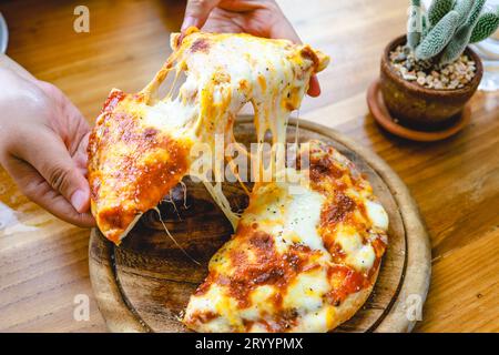 Eine Scheibe frischer, heißer, sehr käsiger vegetarischer Pizza, Mozzarella. Italienische Pizza Margherita in der Hand Stockfoto