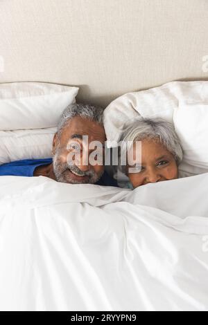 Porträt eines glücklichen älteren, birassischen Paares, das zu Hause im Bett unter der Bettwäsche liegt, Kopierraum Stockfoto