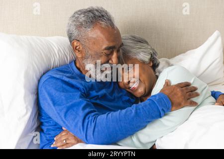 Glückliches älteres, birassisches Paar, das zu Hause im Bett liegt und sich umarmt Stockfoto