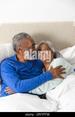 Glückliches älteres, birassisches Paar, das zu Hause im Bett liegt und sich umarmt Stockfoto