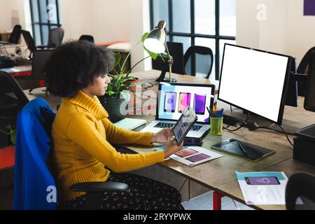 Fokussierte afroamerikanische Designerin, die Tablet und Computer nutzt, mit Kopierbereich am Schreibtisch im Büro. Kreatives Business, Design, Technologie und Freizeit Stockfoto