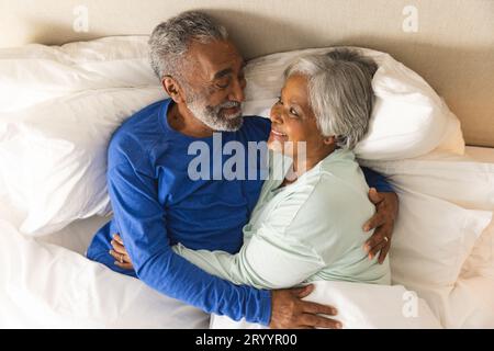 Glückliches älteres, birassisches Paar, das im Bett liegt und sich zu Hause umarmt Stockfoto
