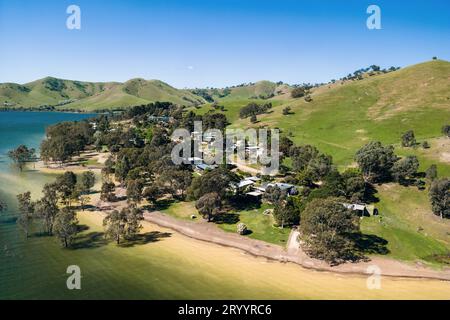 Ein Blick aus der Vogelperspektive auf eine kleine Häusergruppe am Sandufer des Lake Eildon, eingebettet zwischen Gummibäumen. Stockfoto