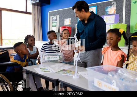 Glückliche, vielfältige Lehrer und Kinder mit Ökologiegegenständen in der Grundschule Stockfoto