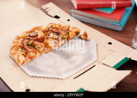Ein Stück Pizza auf dem Tisch. Pizza auf dem Tisch mit Büchern und Getränken für Studenten, die nach der Prüfung feiern. pizz abschneiden Stockfoto