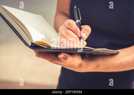 Nahaufnahme einer jungen Frau, die Briefe in Notizblock aufschrieb, um mit der Hand Notizen an ihrem Tagebuch zu machen. Business- und Lifestyle-Concept Stockfoto