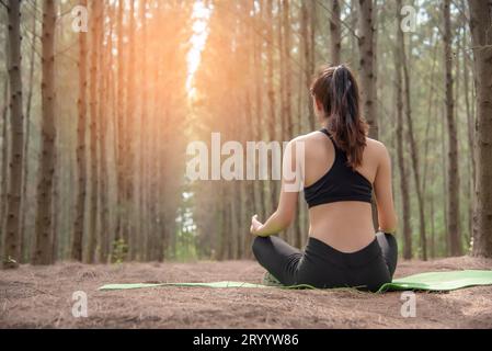 Schöne asiatische junge Frau, die auf grüner Matte liegt und Yoga im Wald macht. Übung und Meditationskonzept. Friedlich und landschaftlich Stockfoto