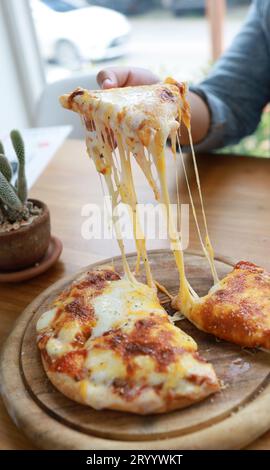 Eine Scheibe frischer, heißer, sehr käsiger vegetarischer Pizza, Mozzarella. Italienische Pizza Margherita in der Hand Stockfoto