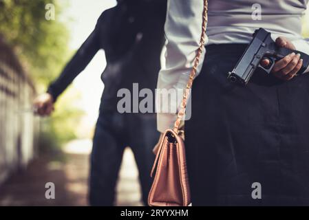 Verschlossen von einer Frau, die eine Handpistole im Rücken versteckt hat, weil sie kämpft, um sich zu räubern oder sich vor gestohlenen Geldern zu schützen oder gefährlich zu sein. Crimina Stockfoto