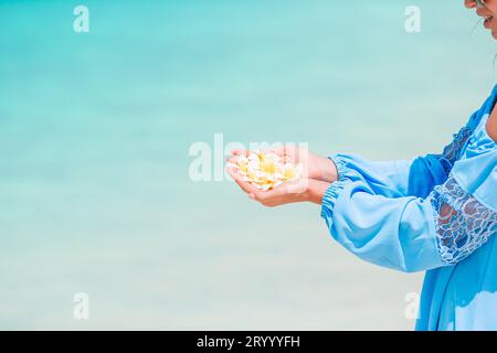 Schöne Frangipani Blumen in den Händen Hintergrund türkisfarbenes Meer auf weiß Strand Stockfoto