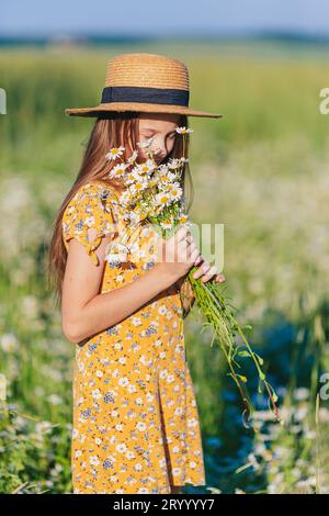 Porträt eines Mädchens in gelbem Kleid und Strohhut auf einem Kamillenfeld im Sommer Stockfoto