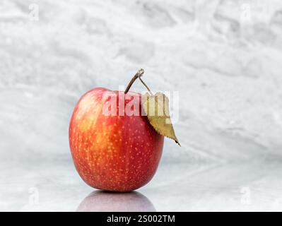 Roter Apfel (Gala-Sorte) mit Blatt auf grau polierter Marmoroberfläche. Hintergrund Stockfoto