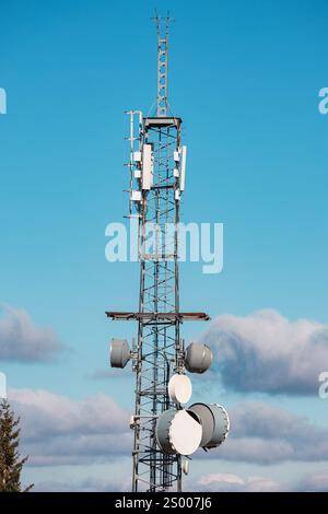 Telekommunikationsturm mit Antennen und Satellitenschalen, hoch stehend vor einem Hintergrund von blauem Himmel und weißen Wolken Stockfoto