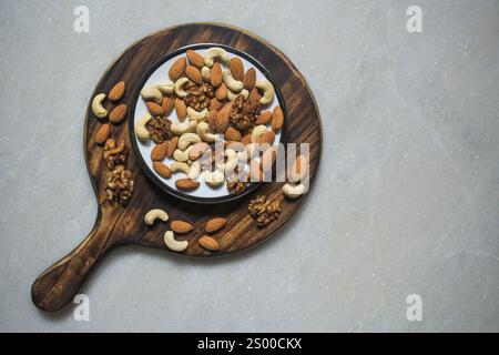 Trockene Früchte, Mandel, Cashews, Walnüsse serviert auf einer weißen Keramikplatte auf einem Holzbrett mit weißem Marmorhintergrund Stockfoto