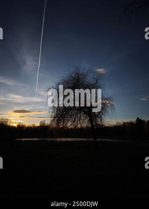 Das Flugzeug verlässt Kondensstreifen über einem Bagr-See bei Sonnenuntergang in Stromovka ceske budejovice, tschechien Stockfoto