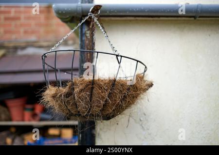 Leerer hängender Blumenkorb mit natürlicher Einlage vor einem Wandhintergrund. Stockfoto