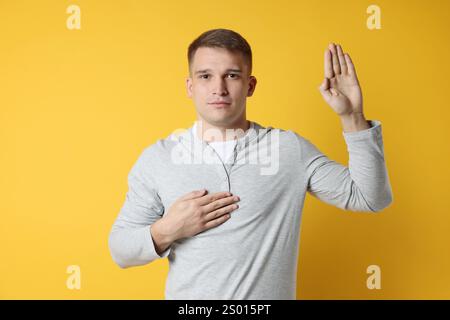 Mann, der Versprechen macht, mit erhobener Hand auf orangem Hintergrund. Eid-Geste Stockfoto