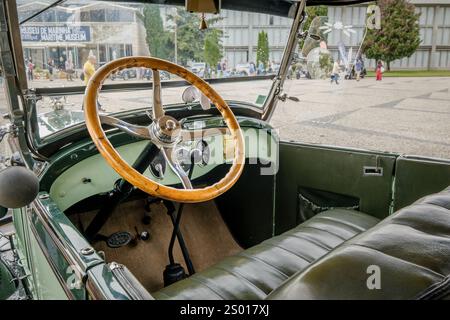 Lissabon, Portugal - 15. Oktober 2023: Grünes Interieur mit Lenkrad und Armaturenbrett des alten Ford A Tudor Limousine. Lenkrad aus Holz und Armaturenbrett aus Vollmetall im selektiven Fokus. Stockfoto