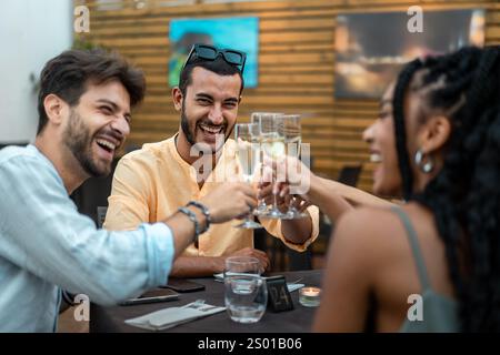 Fröhliche Gruppe von Freunden, die bei einem Abendessen im Freien mit Sektgläsern anstoßen, eine festliche Atmosphäre und gemeinsame Momente genießen. Stockfoto