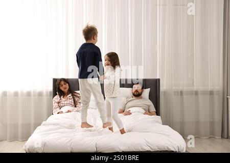 Überforderte Eltern und ihre verspielten Kinder zu Hause im Bett Stockfoto