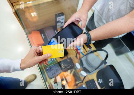 Einzelhandelsmitarbeiter, der das Smartphone in der Nähe des Kunden überprüft und am Point of Sale per kontaktloser Kreditkartentransaktion bezahlt Stockfoto