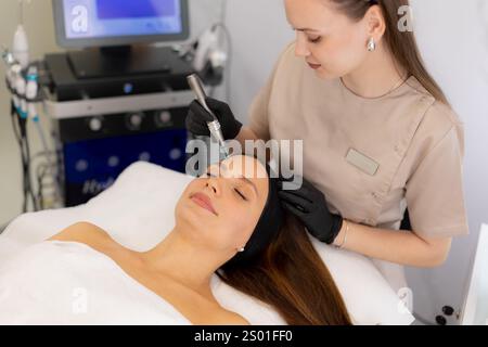 Ein erfahrener Fachmann verwendet ein Mikroneedling-Mesotherapie-Gerät bei einem Patienten in einer ruhigen Klinik, wobei der Schwerpunkt auf Hautverjüngung und Schönheitssteigerung liegt. Die Stockfoto