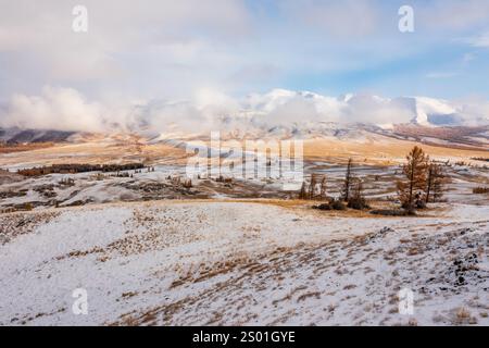 Ruhige, im Herbsttal bedeckte Schneeflächen, umgeben von weit entfernten nebeligen Bergen. Ruhige Wildnis mit karger Vegetation, saisonale Landschaft, die die Schönheit der Natur während der Jahreszeiten veranschaulicht Stockfoto