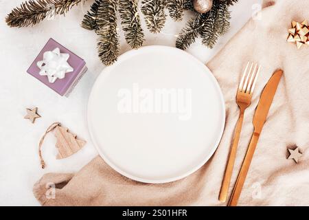 Flacher festlicher Tisch mit leerem Teller, goldenem Besteck, Tannenzweigen und Weihnachtsdekoration. Draufsicht, Kopierraum. Stockfoto