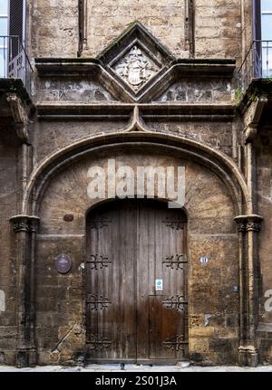 Eine alte Holztür in einer verwitterten Steinmauer mit kunstvollen architektonischen Details und einem dekorativen Emblem über der Tür. Die Struktur hat Stockfoto