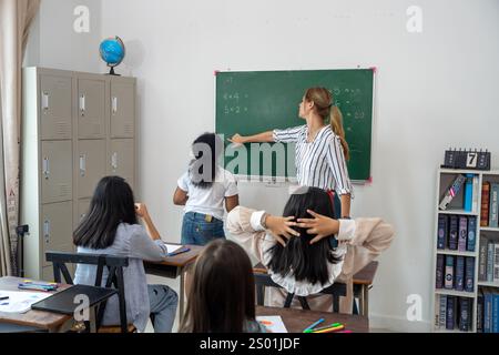 Ein Lehrer führt die Schüler bei der Lösung von mathematischen Problemen an einem Schwarzen Brett in einem gut beleuchteten Klassenzimmer. Die Schüler scheinen motiviert zu sein und konzentrieren sich auf die Lektion Stockfoto