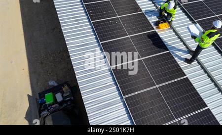 Zwei Arbeiter in reflektierenden Westen und Schutzhelmen installieren Solarpaneele auf einem Dach. Sie verwenden Werkzeuge und konzentrieren sich darauf, die Bedienfelder zu schützen Stockfoto