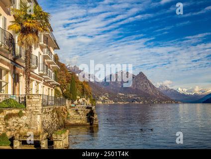 Fantastische Winterlandschaft am Luganer See mit schneebedeckten Bergen. Irgendein Gebäude mit Pier, Enten im Wasser Stockfoto