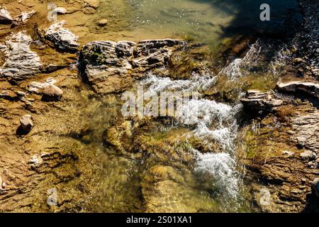 Ein Wasserstrom fließt über Felsen und Kieselsteine. Das Wasser ist klar und die Felsen sind braun Stockfoto