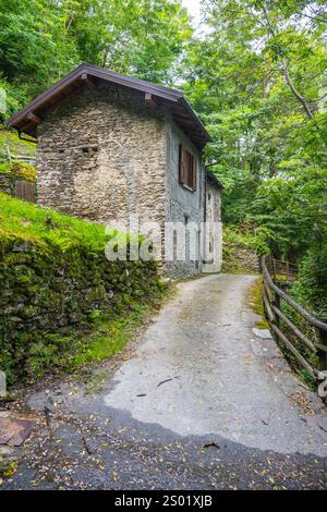 Ein Steinhaus eingebettet in üppiges Grün neben einem gewundenen Pfad, veranschaulicht die Ruhe entlang des Sentiero del Viandante, einem historischen Pfad am Comer See Küste. Stockfoto