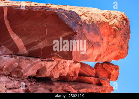 Ein großer Stein mit einem Riss darin. Der Felsen ist rot und der Himmel blau. Der Felsen ist Teil einer Klippe Stockfoto